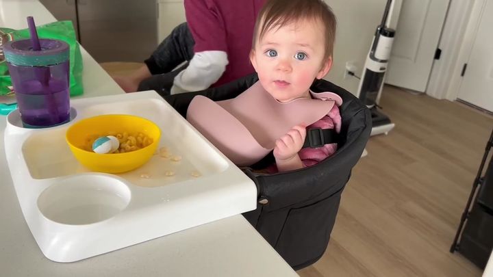 Baby sitting in the clip-on dining chair at a table with a bowl of cereal