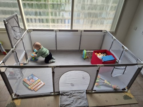 Customer photo: a baby sitting inside the grey playpen with toys and a play mat