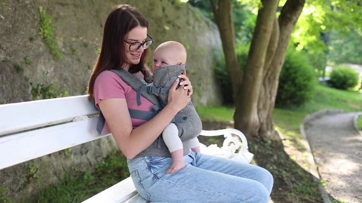 Woman sitting on a park bench wearing the carrier with a baby