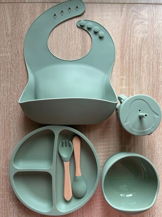 Customer photo: the silicone baby feeding set in sage green laid out on a wooden surface