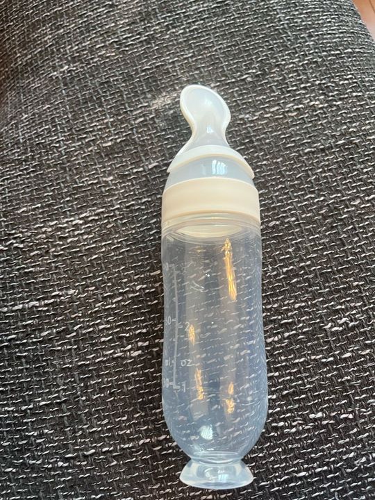 Customer photo: the squeeze feeder lying on a grey sofa, showing the ml and oz markings