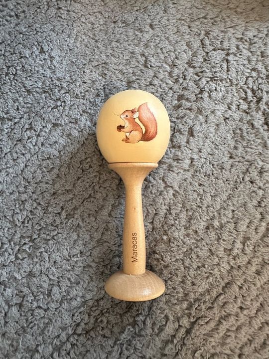 Customer photo: a wooden maraca resting on a grey fleece rug