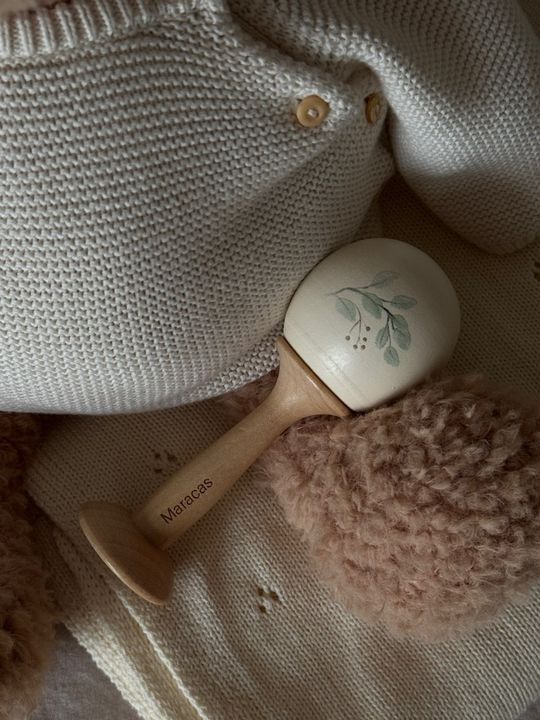 Customer photo: a wooden maraca on a knit cardigan and blanket